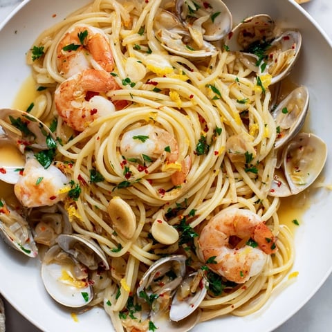 Steaming Seafood Pasta Aglio e Olio with plump shrimp and open clams, glistening with olive oil.