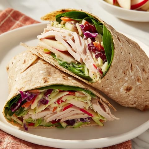 A colorful cranberry apple slaw turkey wrap, ready to eat, served with fresh baby spinach on a plate.