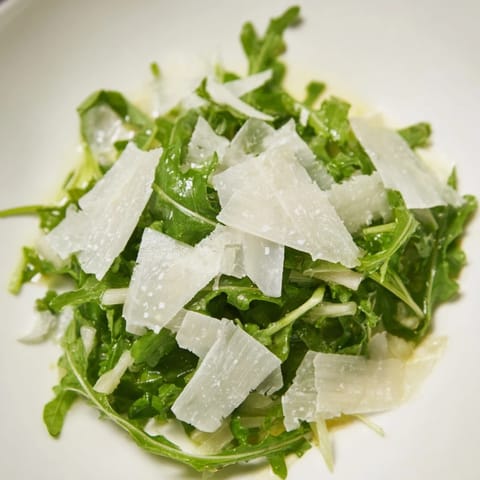 This vibrant arugula salad features peppery greens coated in tangy lemon dressing, a quick, easy Italian dish.