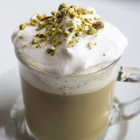 A tall glass of homemade Pistachio Latte, featuring frothy cold foam and garnished pistachios.