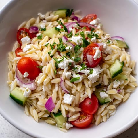 This refreshing Greek Orzo Salad showcases chilled orzo pasta tossed with crisp vegetables, briny Kalamata olives, and fresh herbs, perfect for a summer side dish.