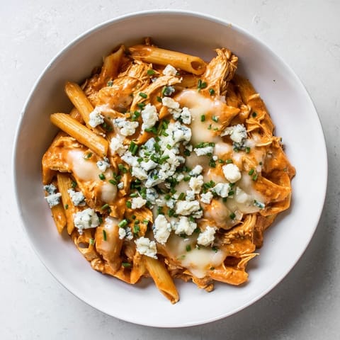 Golden Buffalo Chicken Pasta served in a white bowl, topped with crumbled blue cheese and fresh chives.