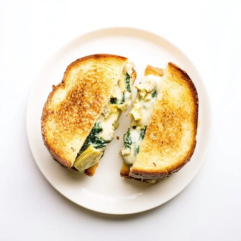 Steaming spinach artichoke grilled cheese on a plate, perfect with a bowl of tomato soup for dipping.