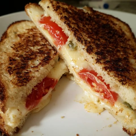 Close-up of a spicy grilled cheese with pepper jack cheese and fresh tomatoes between two buttery, golden-brown slices of jalapeño bread.
