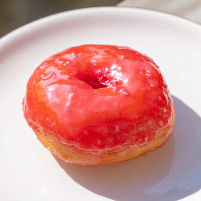 Small, fluffy mini pączki with a sweet, vibrant cherry glaze topping – a perfect dessert.