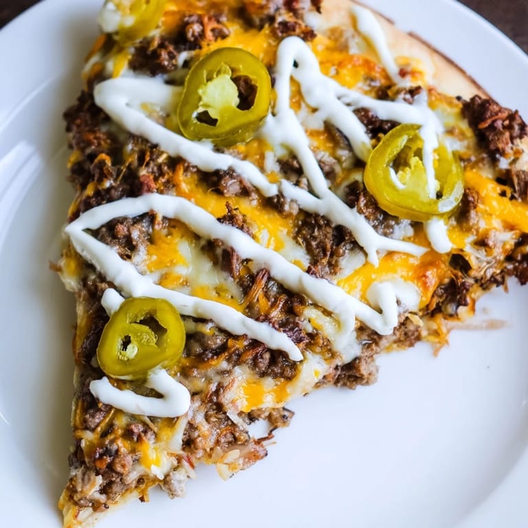 Close-up of a bubbling Ground Beef Taco Pizza garnished with sour cream and fresh, colorful toppings.
