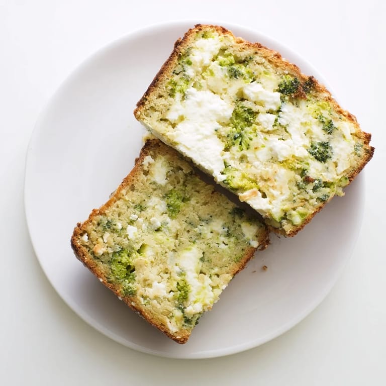 Warm slice of broccoli and feta loaf served with creamy tomato soup, showcasing moist interior and crumbled cheese.