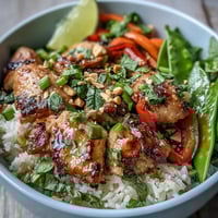 Fragrant Thai Chicken Coconut Bowl garnished with cilantro, peanuts, and lime wedges on a rustic wooden table.